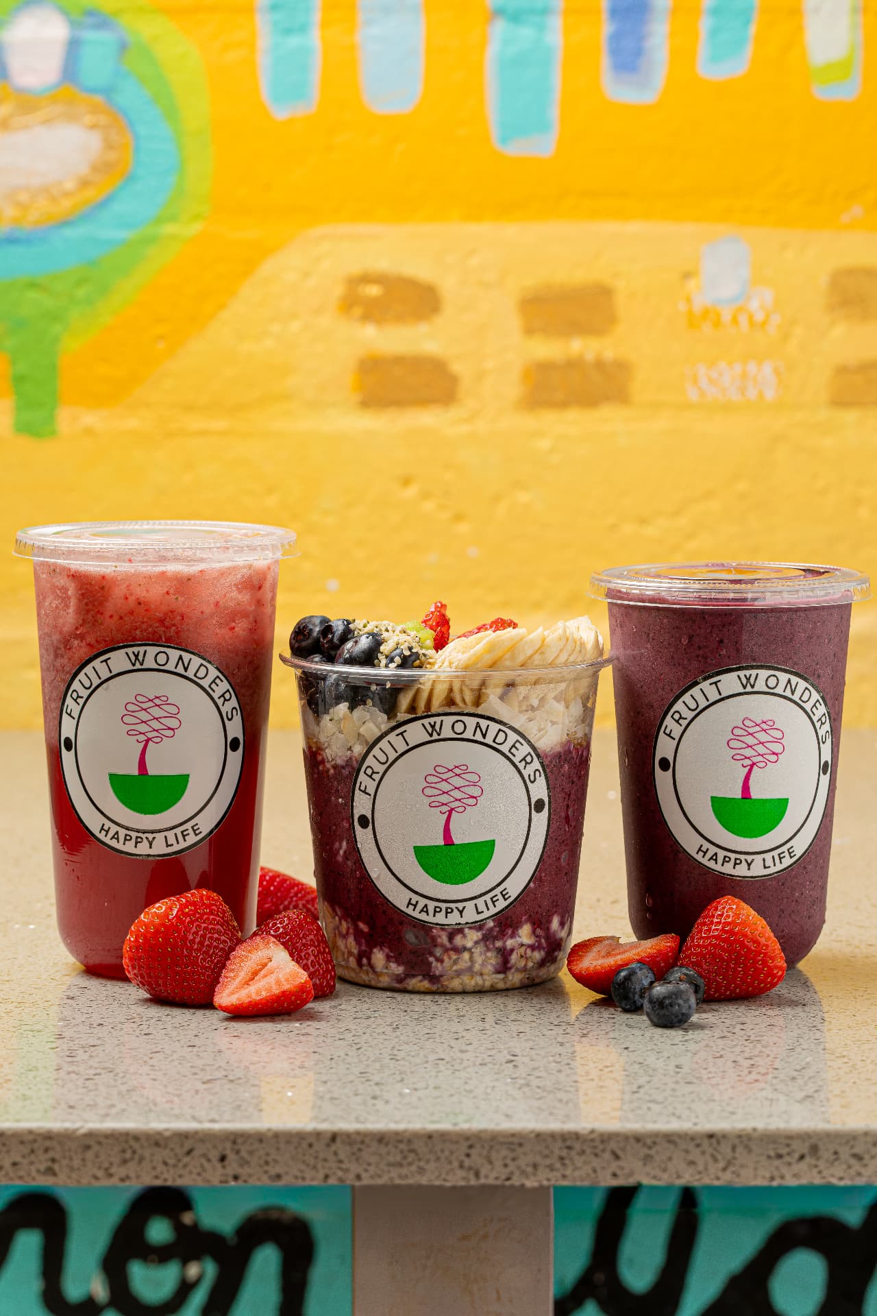 Fruit Wonders smoothies in branded cups in front of a colorful yellow mural